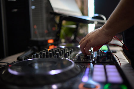 control DJ for mixing music with blurred people dancing at party in nightclub.