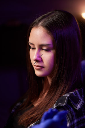 Closeup of a young womans visage with piercing hanging from her nose.