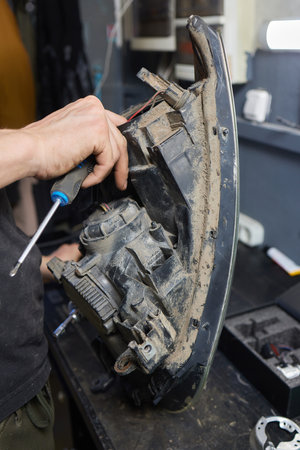 Person fixing Automotive lighting with screwdriver on Motor vehicle headlight
