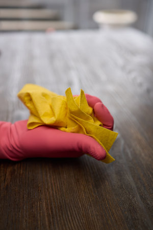 Person in pink gloves cleans wooden table with yellow clothの写真素材