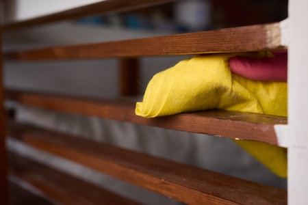 Person in pink gloves cleans wooden table with yellow clothの写真素材