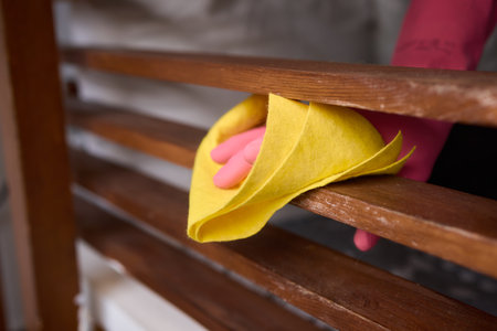 Person in pink gloves cleans wooden table with yellow clothの写真素材