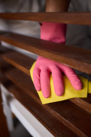 Person in pink gloves cleans wooden table with yellow cloth