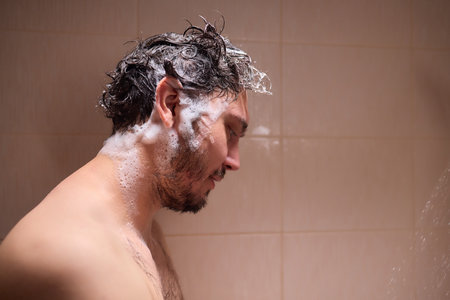 Man washing hair with shampoo in shower, creating foamy lather - personal hygiene care.の写真素材