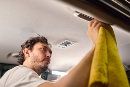 A man is cleaning the cars ceiling meticulously with a yellow cloth, focusing on detailの写真素材