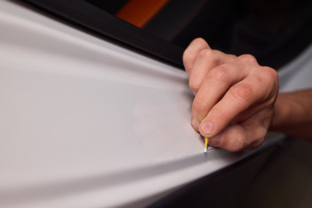 A man repaints a scratch on a car part in an auto repair shop with precision and craftsmanshipの写真素材