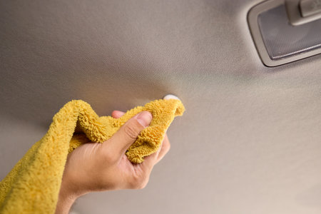 A man is cleaning the cars ceiling meticulously with a yellow cloth, focusing on detailの写真素材