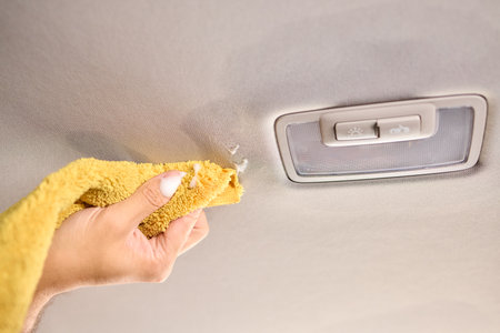 A man is cleaning the cars ceiling meticulously with a yellow cloth, focusing on detailの写真素材