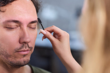 A man is having his eyebrows groomed by a professional beautician using tweezersの写真素材