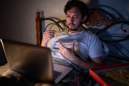 Feeling cozy in bed with a latenight snack, browsing on laptop for a relaxing time