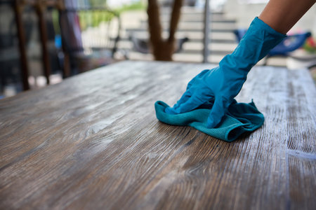 Professional cleaning service provider wearing gloves, meticulously wiping wooden surface