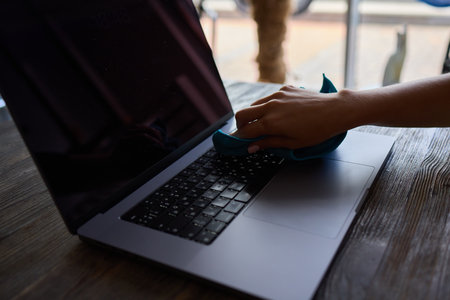Person Cleaning Laptop Keyboard with Gloves and Cloth, Taking Precautions for Health and Hygieneの写真素材