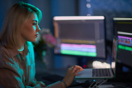 Professional Video Editor Working Late on Advanced Editing Software in Home Officeの写真素材