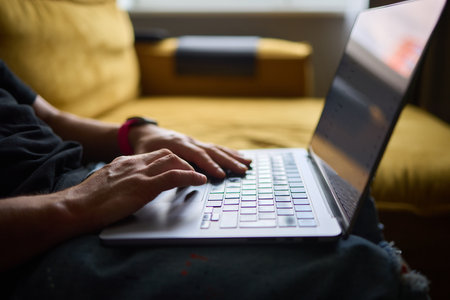 A person is happily typing on a laptop while sitting comfortably in a cozy living room settingの写真素材