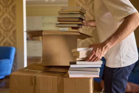 A man organizes his book collection in a new home, creating a comfortable, minimalist setupの写真素材
