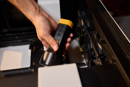 A man cleans a computer case with a vacuum in a bright room, stressing workspace tidinessの写真素材