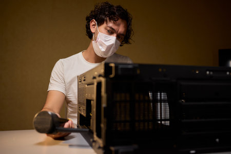 A man cleans a computer case with a vacuum in a bright room, stressing workspace tidiness
