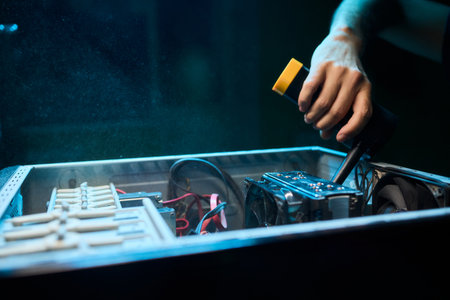 A man cleans a computer case with a vacuum in a bright room, stressing workspace tidinessの写真素材