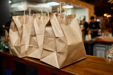 There are three craft paper bags placed neatly on a rustic wooden counter inside a cafe settingの写真素材
