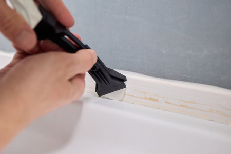 A hand skillfully using a tool on the edge of a pristine bathtub in a bright bathroomの写真素材