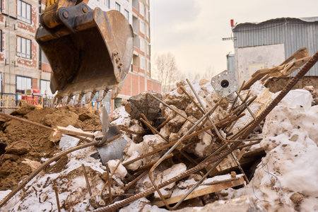 An excavator is digging through construction debris in an urban setting, assisting the task