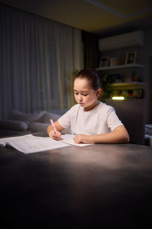 A young child is deeply engaged in thought while completing their homework during a late nightの写真素材