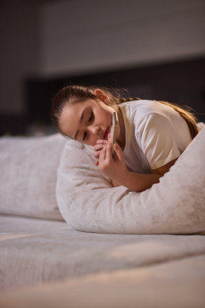 A Young Girl Completely Engaged with Her Smartphone in a Cozy and Comfortable Settingの写真素材