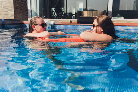 Two women, one Caucasian and an Asian in the pool. The blonde woman wrap the other with the pride...