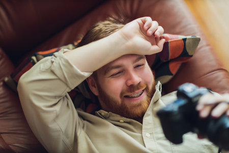 Happy man viewing pictures on screen camera while relaxing together on red sofa in modern house.