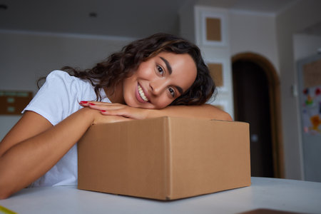 Happy woman unpacking container at home, opening carton box, looking inside package. Smiling satisfied customer receiving parcel from order delivery service, unboxing purchase.の写真素材