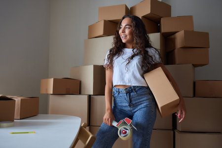 Happy woman unpacking container at home, opening carton box, looking inside package. Smiling satisfied customer receiving parcel from order delivery service, unboxing purchase.の写真素材