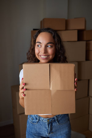 Happy woman unpacking container at home, opening carton box, looking inside package. Smiling...