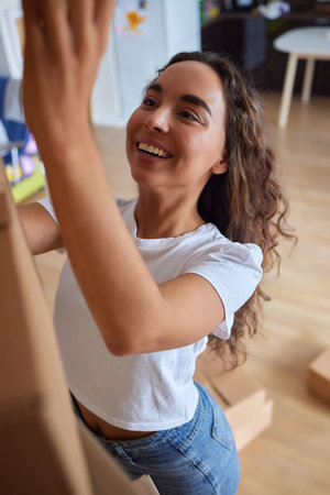 Happy woman unpacking container at home, opening carton box, looking inside package. Smiling satisfied customer receiving parcel from order delivery service, unboxing purchase.の写真素材