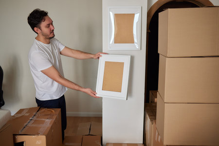 A young man looking through a moving box, filled with clothes, books and a picture frame.の写真素材