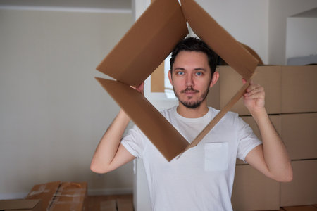 Man standing in living room on day of move to rented home, unbox carton box with belongings.