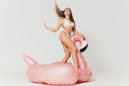 Portrait of slim graceful girl with short blonde hair on pink inflatable flamingo. Gorgeous cheerful young woman in bikini having fun, waiting for party.の写真素材