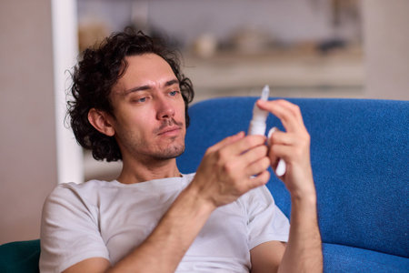 A Man Using an Inhaler While He is Relaxing Comfortably at Home in a Cozy Environmentの写真素材