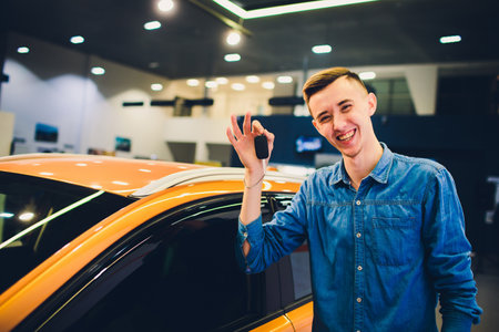 An Excited Young Man Joyfully Holding Car Keys in Front of His Brand New Vehicleの写真素材