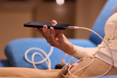 A person is engaged with their smartphone while surrounded by various charging cablesの写真素材