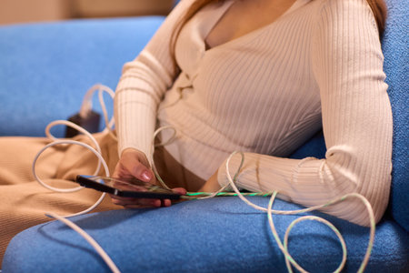 A person is engaged with their smartphone while surrounded by various charging cablesの写真素材