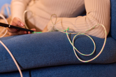 A person is engaged with their smartphone while surrounded by various charging cables