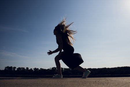 A woman is jogging while enjoying the beautiful clear blue sky aboveの写真素材