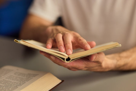 Hands purposefully engaged with an engrossing book carefully placed on a table surfaceの写真素材