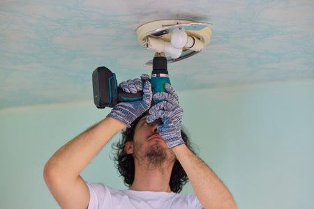 A person is installing a ceiling light fixture using a power tool with great care and skillの写真素材