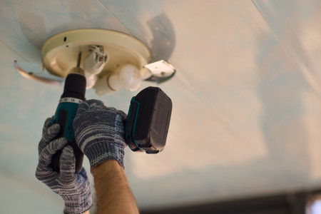 A person is installing a ceiling light fixture using a power tool with great care and skillの写真素材