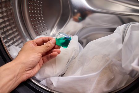 A hand is holding a colorful laundry pod as it is placed into a washing machine for cleaningの写真素材