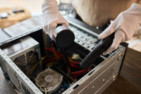 A man cleans a computer case with a vacuum in a bright room, stressing workspace tidiness