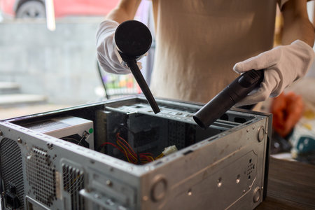 A man cleans a computer case with a vacuum in a bright room, stressing workspace tidinessの写真素材