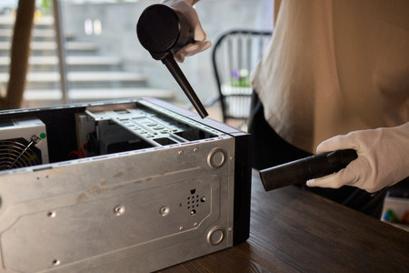 A man cleans a computer case with a vacuum in a bright room, stressing workspace tidinessの写真素材