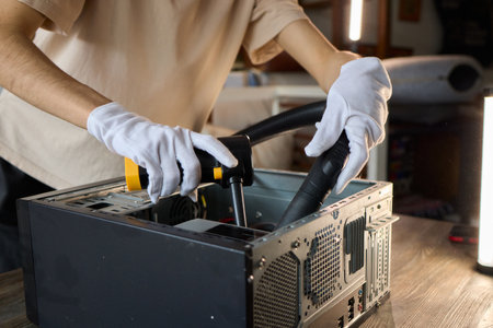 A man cleans a computer case with a vacuum in a bright room, stressing workspace tidinessの写真素材